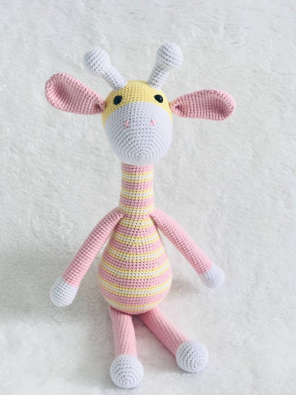 This is an instantly eye-catching a crocheted pink and yellow giraffe with a white horn! The giraffe appears to have been made from soft, colorful yarn that's been cleverly shaped and manipulated by skilled hands into its gentle curves.