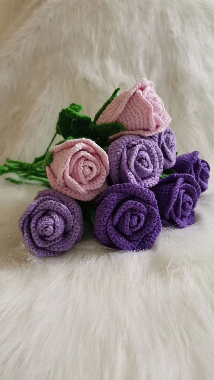 Close-up of handmade crochet roses in a variety of colors, including red, yellow, purple, and pink. The petals are intricately crocheted and feature a soft texture. The center of each rose is a contrasting color and has a raised, textured appearance.