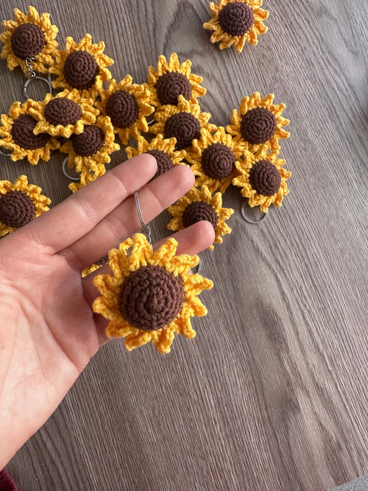 A handmade crochet keyring shaped like a bright yellow sunflower with a brown center.