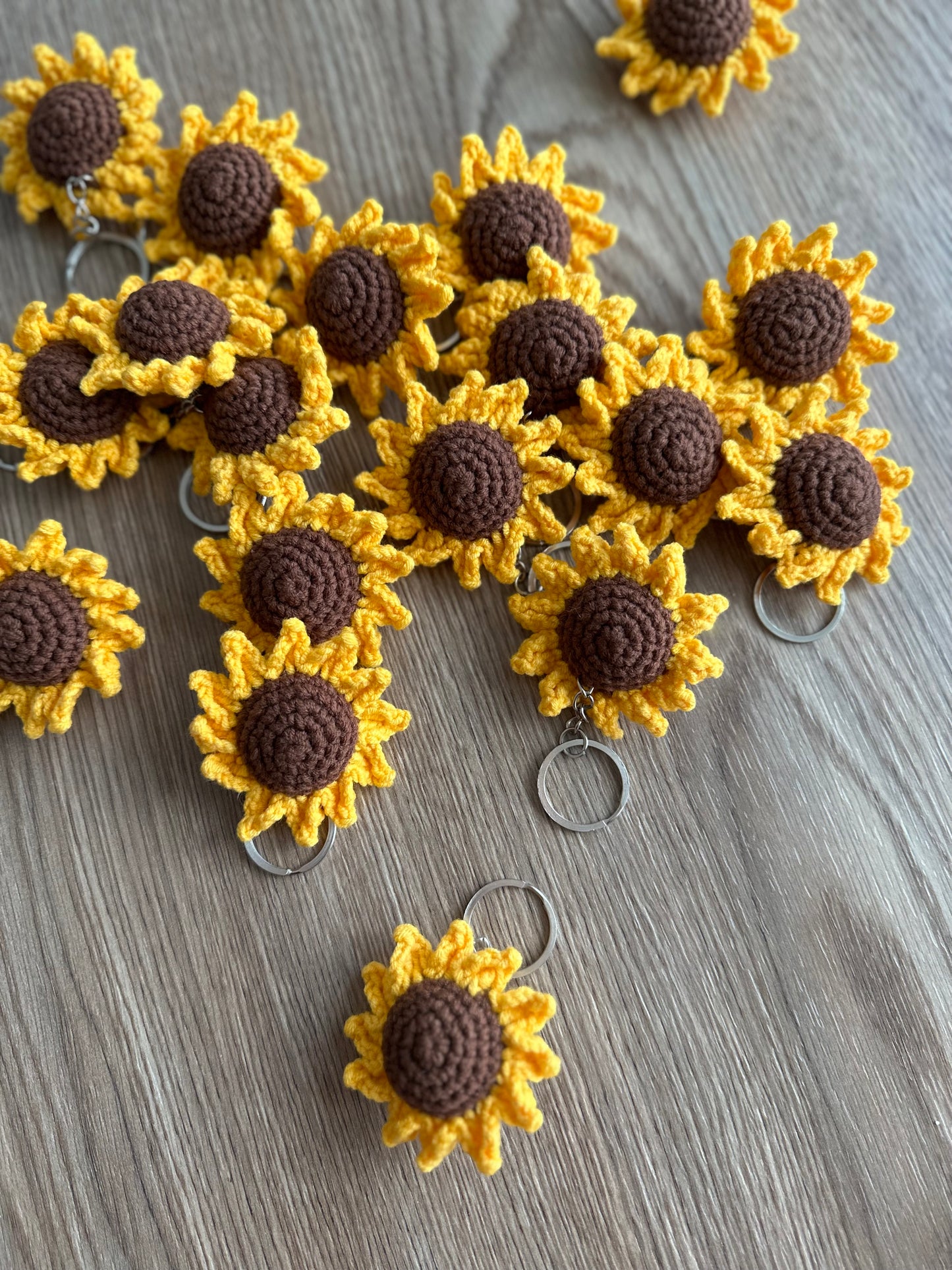 A detailed close-up of a crocheted sunflower keyring, showcasing the texture of the yellow and brown yarn.
