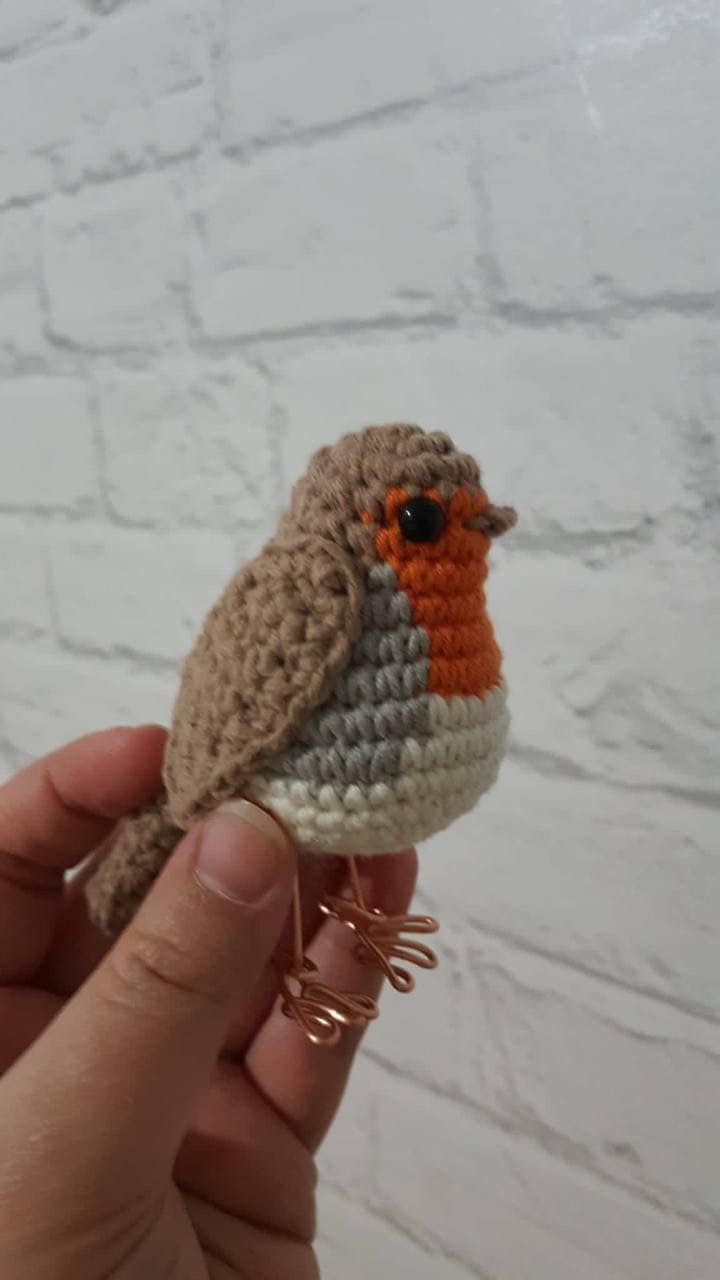 crochet red robin with copper wire feet standing. The robin has a round plump body with a red breast, brown wings and a brown beak. Its eyes are black. The copper wire feet are visible and add a unique touch to the handmade bird.