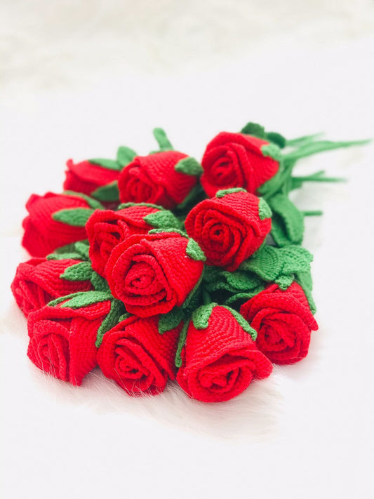 Close-up of handmade crochet roses in a variety of colors, including red, yellow, purple, and pink. The petals are intricately crocheted and feature a soft texture. The center of each rose is a contrasting color and has a raised, textured appearance.