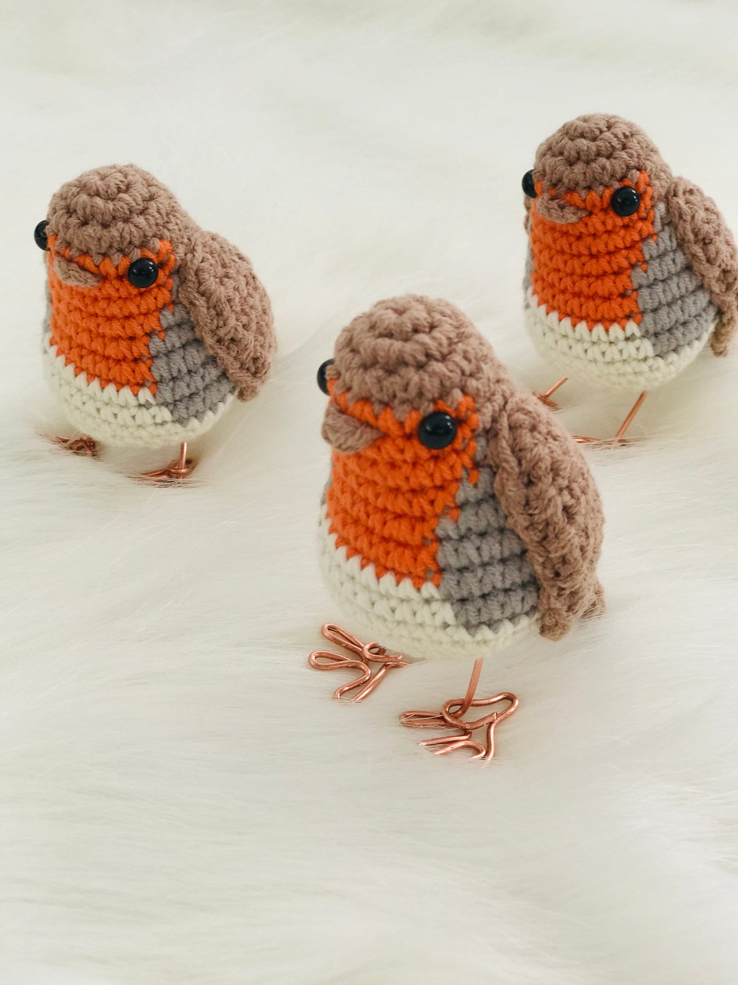 crochet red robin with copper wire feet standing. The robin has a round plump body with a red breast, brown wings and a brown beak. Its eyes are black. The copper wire feet are visible and add a unique touch to the handmade bird.