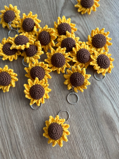A detailed close-up of a crocheted sunflower keyring, showcasing the texture of the yellow and brown yarn.